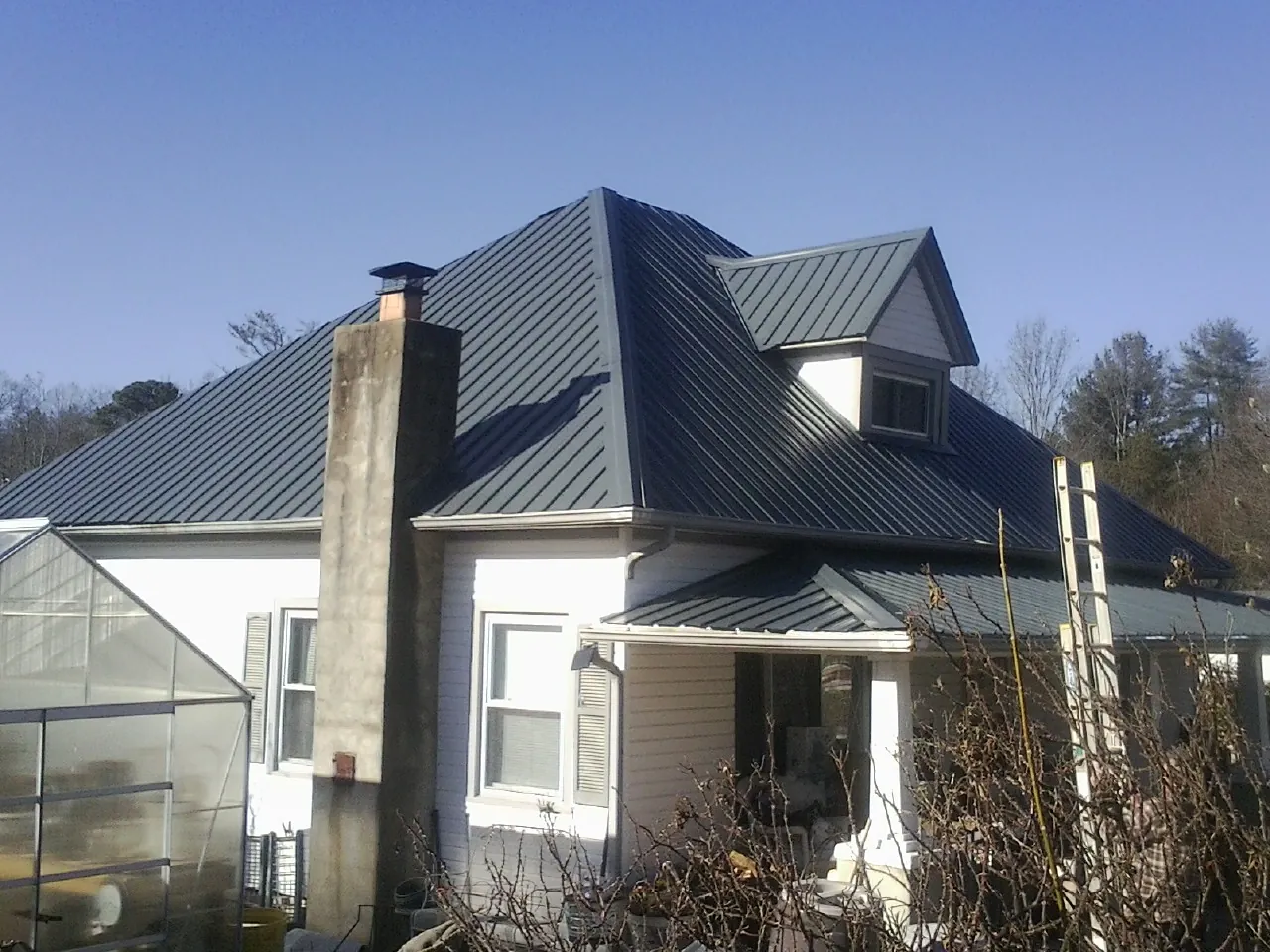 Dark blue standing seam metal roof on a white farmhouse with dormer — Slate & Tile Roof Repair by Roofing Brothers in Prinsburg