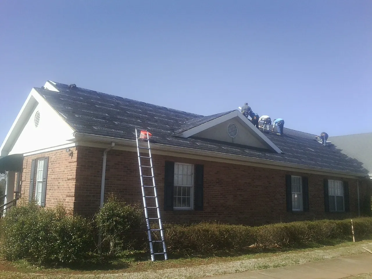 Crew tearing shingles off a brick ranch roof with a ladder set — Emergency Roof Repair work by our crew in Prinsburg