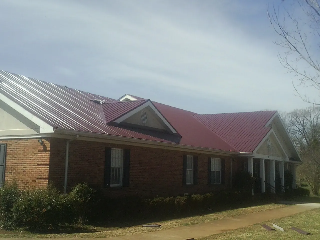 Red metal roof with gabled entries on a long brick building, from a Hail Damage Roof Repair job in Prinsburg