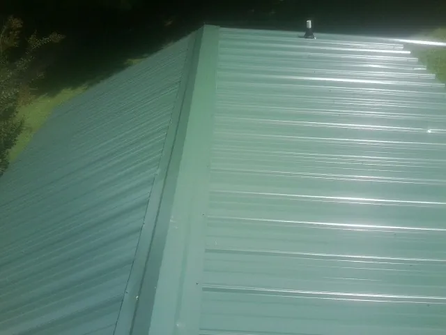 New green metal panels meeting at the ridge of a roof — Flat Roof Repair work by our crew in Prinsburg