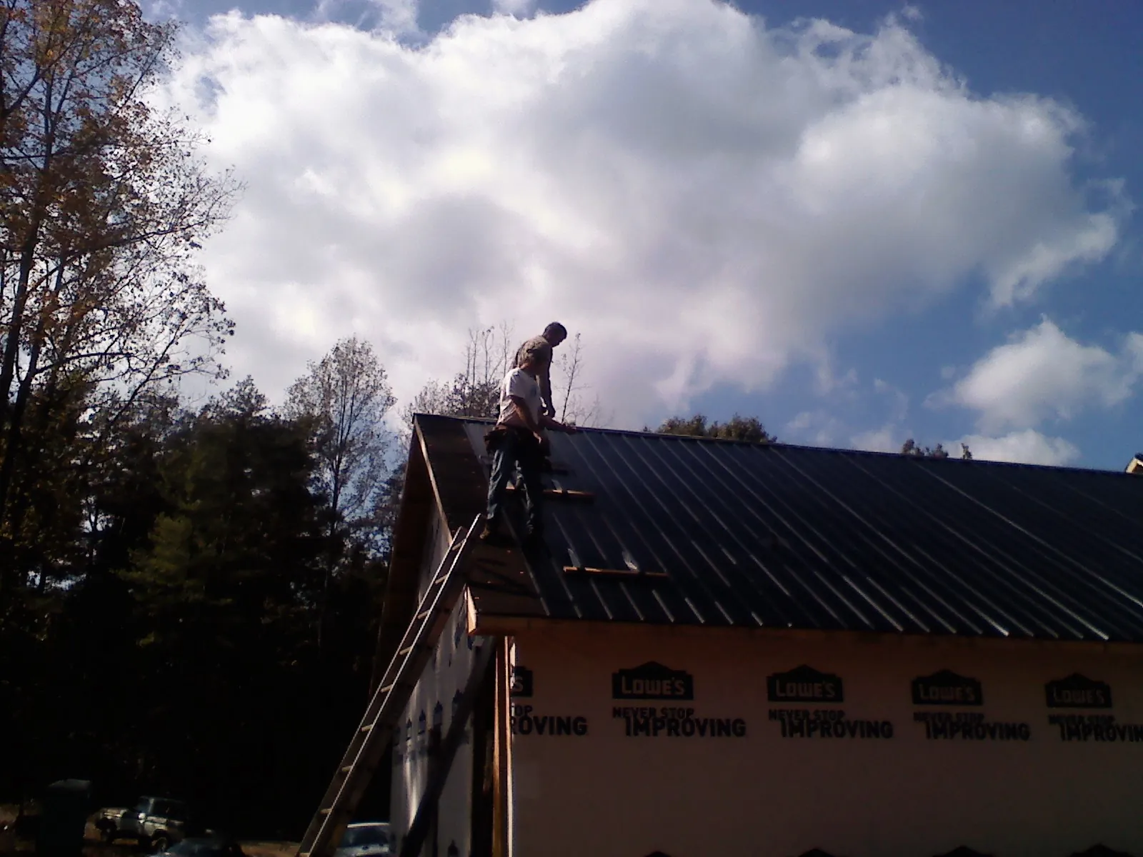 Roofer fastening dark metal panels high against a cloudy sky, from a Roof Inspection job in Prinsburg
