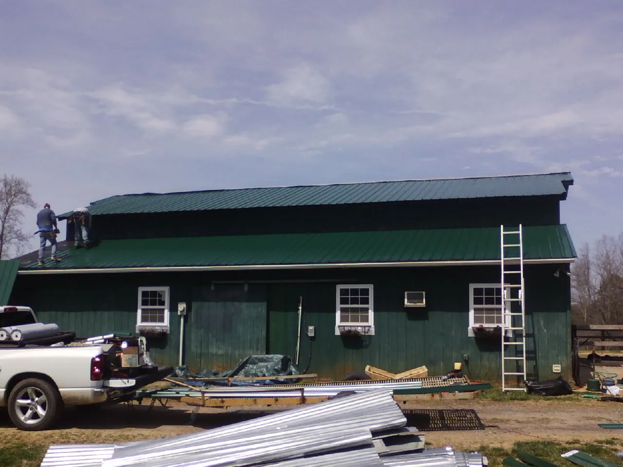 Crew installing green metal roofing on a large green barn in Prinsburg