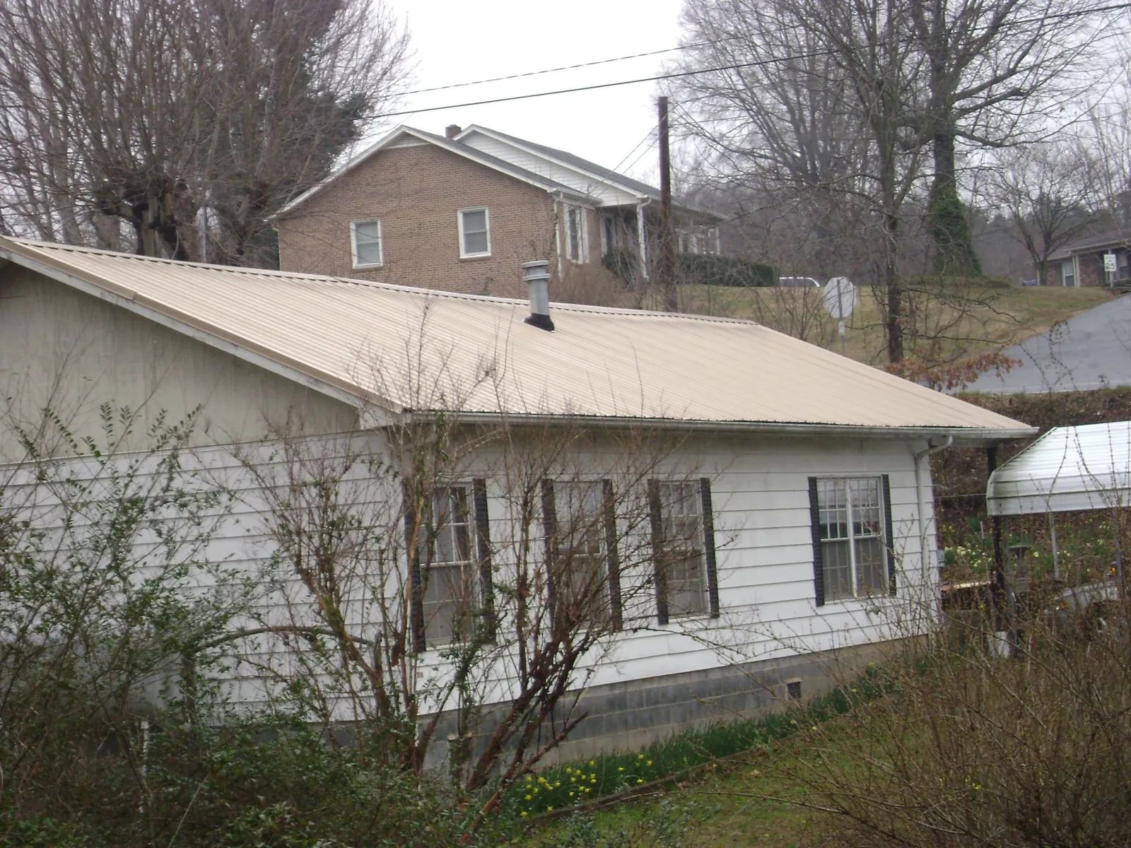 Tan metal roof on a white sided house set into a hillside — Commercial Roofing by Roofing Brothers in Prinsburg