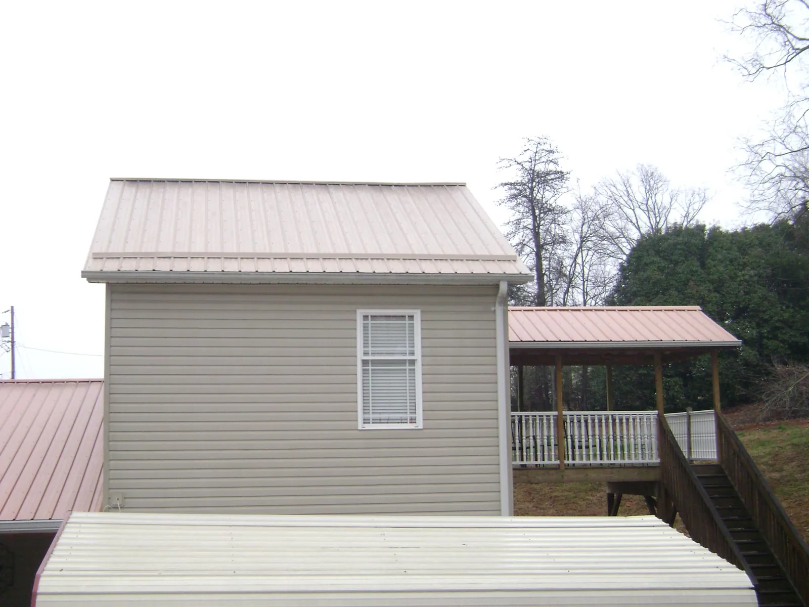 Tan metal roofs on a two story addition and attached porch, from a Roof Replacement job in Prinsburg